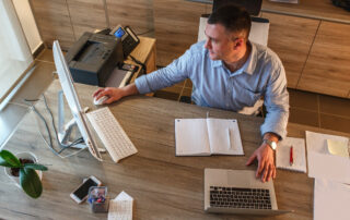 A man sitting at an office desk and working on a computer with a notepad and pen in front of him
